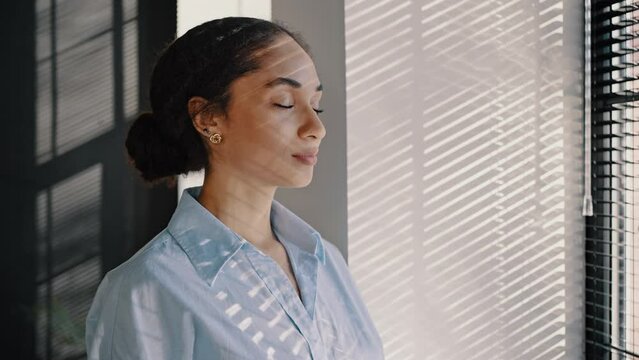 Confident young African American businesswoman taking deep breath, looking through the office window