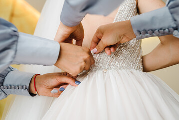 Wedding. Bridesmaids preparing bride for the wedding day. Girls helps fasten a dress the bride before the ceremony. Luxury bridal dress close up. Back of the dress on the bride wearing.