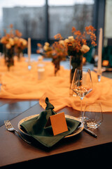 Luxury table setting for a celebration in a restaurant. Dark tones of orange and green are the colors of the holiday. Tableware and catering for the holiday