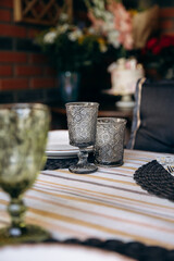 Luxury table setting for a celebration in a gazebo with greenery. Glass dishes, plates and glasses. Preparation for the holiday