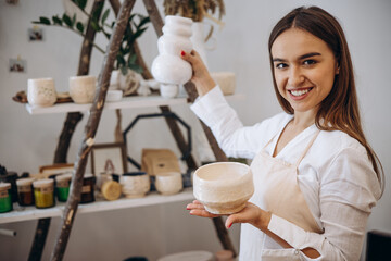 Woman potter holding ceramic bowls at store