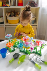 A little girl playing with colorful flower garden toys and planting tools on white table. Garden themed toys for kids. Pretend play, Montessori activity