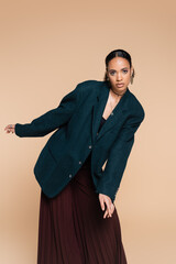 young african american model in dark blue woolen blazer and wide pants posing isolated on beige.