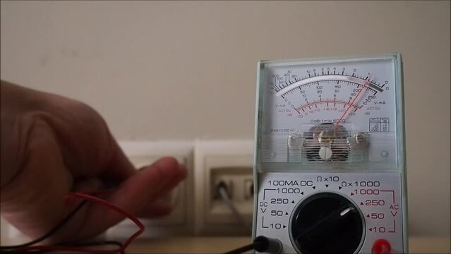 Electrician testing mains electricity outlet with an analog voltmeter. Measuring voltage electric power supply.