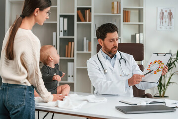 Talking about healthy eating. With baby and mother. Doctor in formal clothes is working in the cabinet