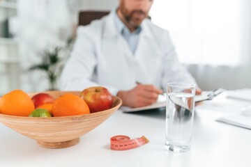 Fruits is on the table. Doctor in formal clothes is working in the cabinet