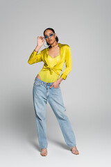 full length of well dressed african american woman in blue sunglasses posing with hand in pocket on...