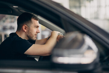 Handsome man sitting in new car in car showroom