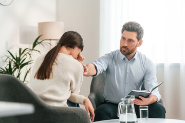 Fototapeta premium Woman is crying on the therapy session. Doctor in formal clothes is working in the cabinet