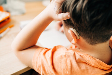 Kid boy with hearing loss wearing hearing device and doing homework. Close-up view