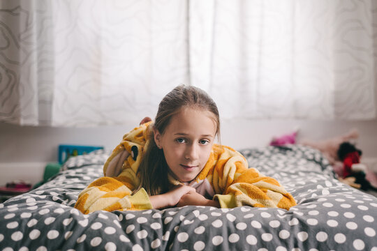 Tween girl in a giraffe onesie lying on her bed, looking to camera