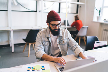 Focused hipster employee using laptop in office