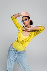 pretty african american woman in blue sunglasses and stylish shirt gesturing isolated on grey.