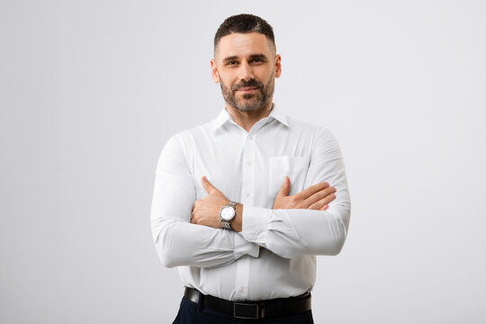 Portrait of handsome middle aged businessman with folded arms standing over grey background and looking at camera