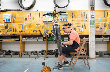 woman fixing bike in community workshop, bike hung with chains and workshop with tidy tools, girl...