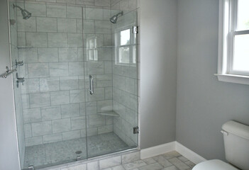 Shower with two shower heads and glass doors, gray tiles for sleek modern look. - obrazy, fototapety, plakaty