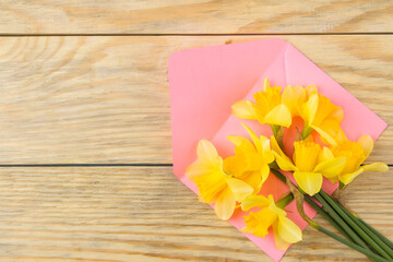 A bouquet of daffodils, spring flowers and a pink envelope. on a natural wooden background. top view
