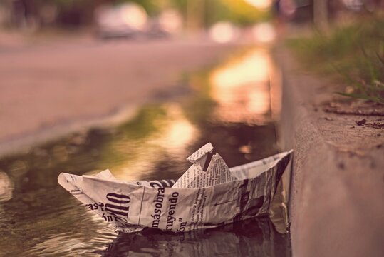 Barco de papel de peri&oacute;dico en la zanja de la acera