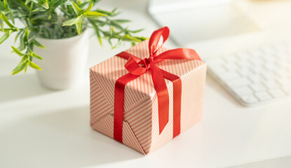 Gift box with red ribbon and hearts on the table near laptop.