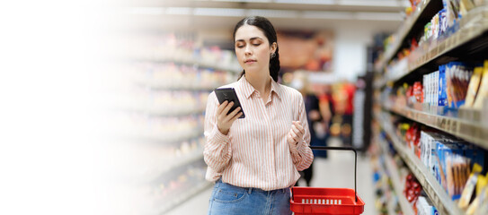 Web banner of shopping with mock up. Young Caucasian woman uses smartphone and holds basket in her hands. Concept of apps for sale in supermarket