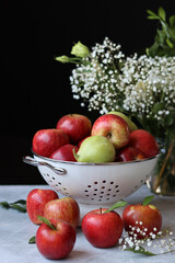 Naklejka na ściany i meble Apples and flowers on a table. Shiny red apples in a colander, Black background. 