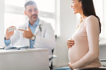 Fototapeta premium Pregnancy and medicine concept. Male gynecologist giving pills to pregnant lady during appointment at hospital