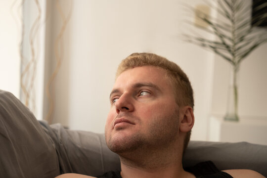 Sad Thoughtful Young Man Lying On Sofa At Home Looking Away.Copy Space.