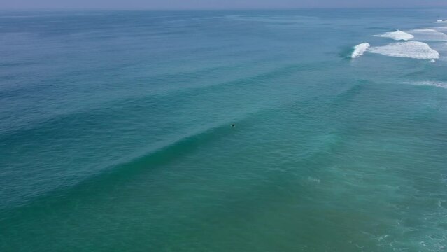 Aerial drone view of surfer sitting on his board watching the waves coming by.