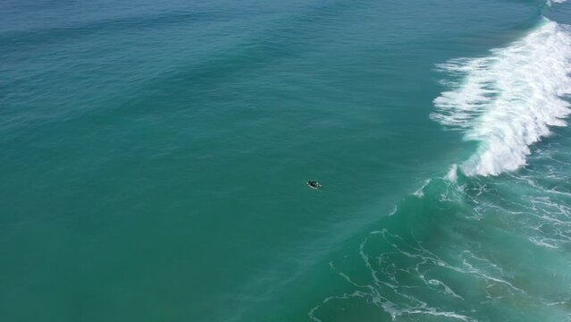 Aerial drone view of surfer sitting on his board watching the waves coming by.