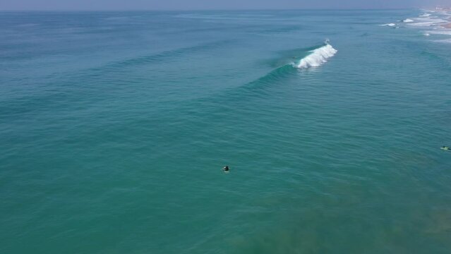 Aerial drone view of surfer sitting on his board watching the waves coming by.