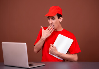 Funny courier in a red uniform sits at his desk. Brown background.