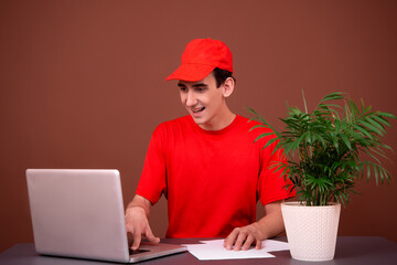 Funny courier in a red uniform sits at his desk. Brown background.