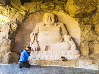 Kalasin, Thailand - February 1, 2023. Buddhist men worship a carved stone Buddha image  at Phu Dan Hai Temple, Kuchinarai District Kalasin Province, Thailand