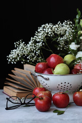 Naklejka na ściany i meble Apples and flowers on a table. Shiny red apples in a colander, Black background. 