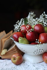 Organic pears and apples in a white metallic colander. Close up photo of seasonal fruit on a table. Colorful still life with apples and Gypsophila flowers.  Natural vitamins and antioxidants concept. 