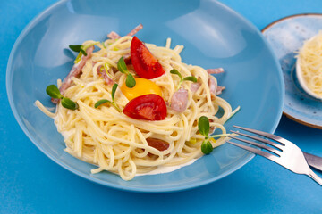 Pasta with cheese and egg, bacon and tomatoes, microgreens. Food in a blue plate. Homemade carbonara pasta. Lunch on the table top view. Italian spaghetti with ham, cream