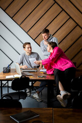 A team of three people is working in the office, communicating and discussing work, looking at notes. IT team in the office, two men and a woman. Young serious entrepreneurs discussing business.