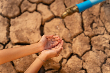 Hand of little girl wating for a drip of water from a faucet at dry ground. Water scarcity and crisis concept.
