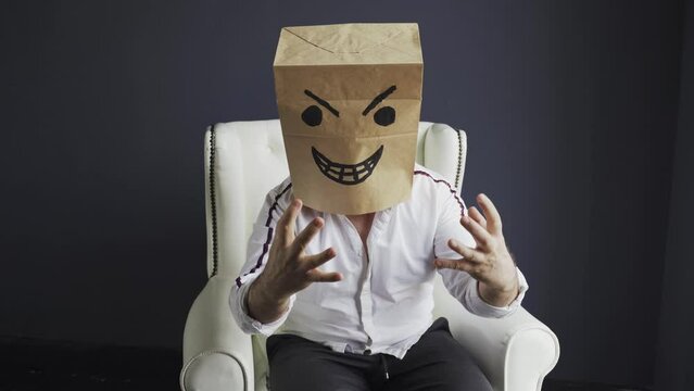 A man with a bag on his head, with an evil smiley face drawn, sits on a white chair, gloats emotionally. Emotions and gestures.