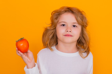 Fototapeta na wymiar Kid with persimmon in studio. Studio portrait of cute child hold persimmon isolated on yellow background.
