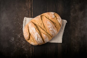 delicious freshly baked bread on kitchen towel on dark brown wooden table