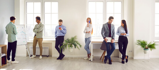 Fototapeta premium Diverse business professionals in modern office workplace. Different people working in office. Young men and women standing in office, talking, discussing work, using mobile phones. Banner background