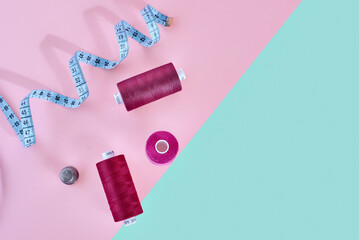 Colored thread rolls and measuring tape for sewing on two tone background. Flat lay