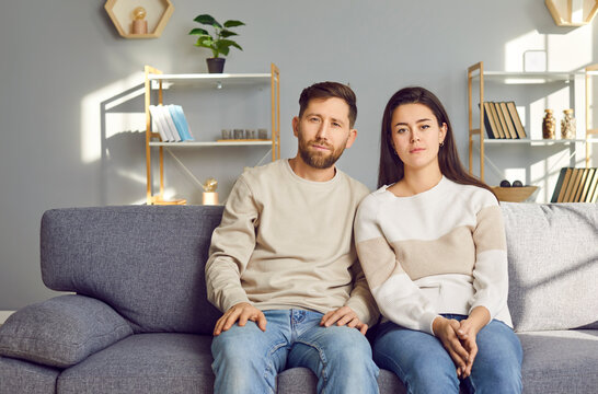 Portrait Of A Young Couple Looking Serious At Camera Making Video Call Together Sitting On Couch At Home Chatting With Friends Online At Webcam. Concept Of Video Call, Internet Connection.