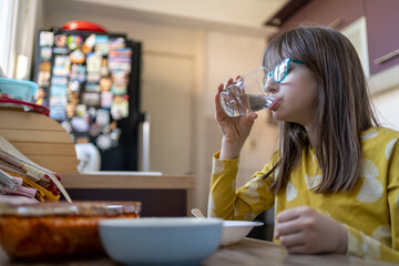 Young girl drinking water near the table with fruits and vegetables in the kitchen. Healthy food, drinks, diet, detox and people concept.
