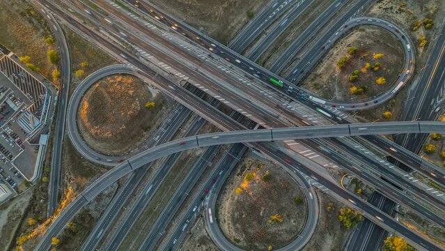 Elevated top view time-lapse of car traffic at multiple lane highway. Aerial view zoom out of highway road intersection and city traffic at sunset. Urban cityscape concept, Spain