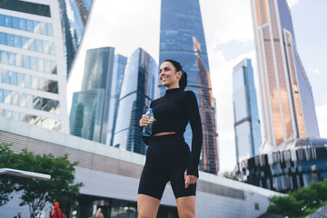 Content young sportswoman with bottle water in city center