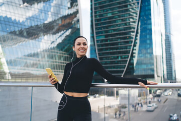 Cheerful standing sportswoman listening to music in earphones