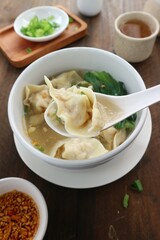 scooping wonton soup from a white bowl