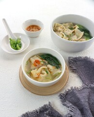two bowls of wonton soup with chili sauce and chopped green onions